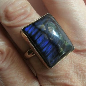 Puede incluir: Un anillo de oro con una gran piedra rectangular de labradorita azul iridiscente.