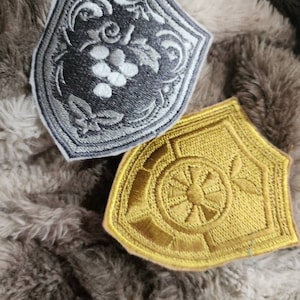 May include: Two embroidered patches, one silver with a grapevine design and the other gold with a sunburst design.