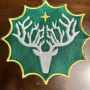 May include: A green and yellow embroidered patch with a white deer silhouette and a gold star in the center.