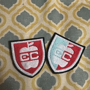 May include: Two embroidered patches with a red apple and the letters "CC" in white. One patch has a red background and the other has a light blue background.