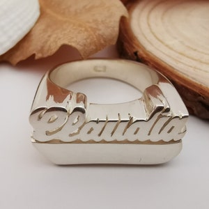 K&ouml;nnte beinhalten: Ein polierter Silberring mit dem Namen Claudia in erhabener Schreibschrift. Der Ring ist dick und massiv gearbeitet und besitzt eine metallische Oberfl&auml;che, die das Licht auf der glatten, geschwungenen Form reflektiert.