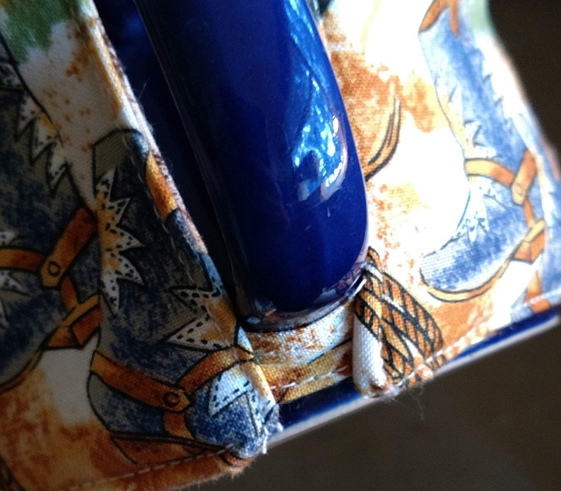 Puede incluir: Una taza de cer&aacute;mica azul con asa, envuelta en una funda de tela con un patr&oacute;n de botas de vaquero. La tela es blanca con detalles marrones y azules.