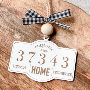Może przedstawiać: Biała drewniana ozdoba choinkowa z czarno-białą wstążką w kratkę, drewnianym koralikiem i tekstem "Christmas 2021", "3734", "Hixson", "Home" i "Tennessee".