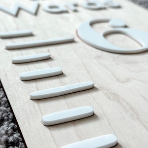 May include: A wooden growth chart with the words "The Word is" and the number "6" in white raised letters. The chart has five white lines for measuring height.