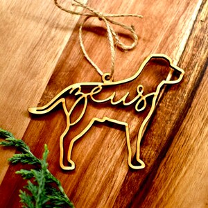 May include: A wooden dog ornament with the name "Zeus" cut out in the design. The ornament is hanging from a piece of twine.