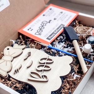 May include: A craft kit for painting a wooden ghost with a bow and the word "Boo" on it. The kit includes paint, brushes, and a card with instructions.