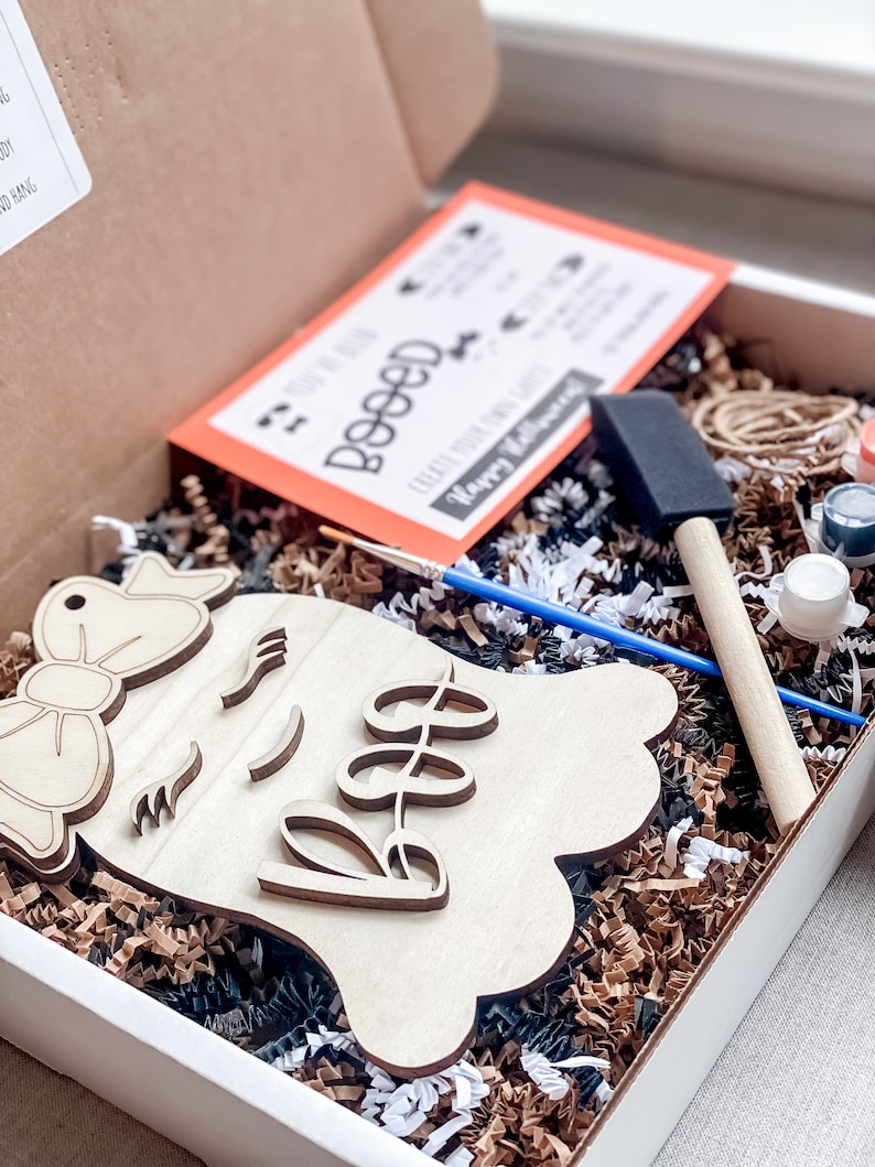 May include: A craft kit for painting a wooden ghost with a bow and the word "Boo" on it. The kit includes paint, brushes, and a card with instructions.