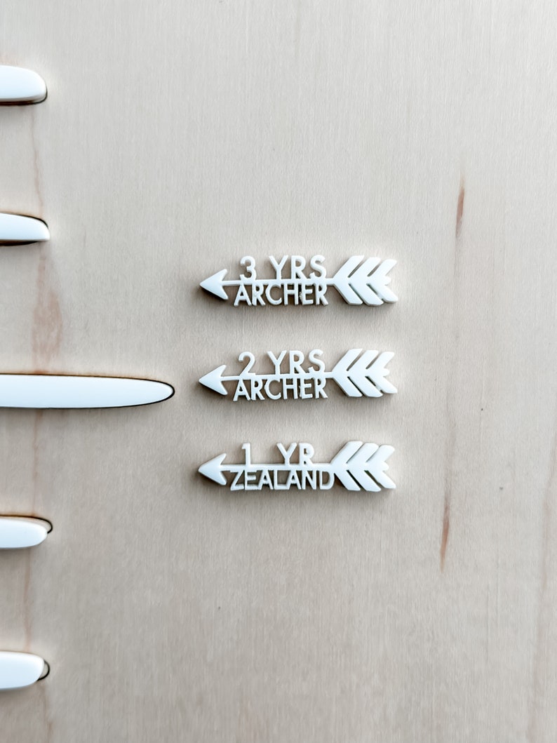 May include: Three white wooden arrows with the text "3 yrs Archer", "2 yrs Archer", and "1 yr Zealand" on a light wood background.