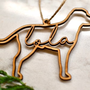 May include: Wooden dog ornament with the name "Lola" cut out inside the silhouette. The ornament is brown and has a string for hanging.