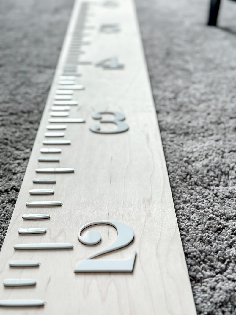 May include: A white wooden growth chart with white numbers, showing the numbers 2, 3, and 4. The chart is on a gray carpet.
