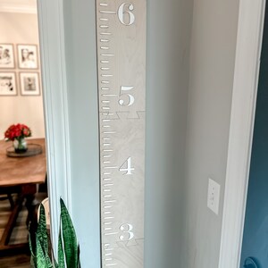 May include: A wooden growth chart with white numbers and the text "The Morgans" at the top. The chart is mounted on a wall and has a light wood finish.