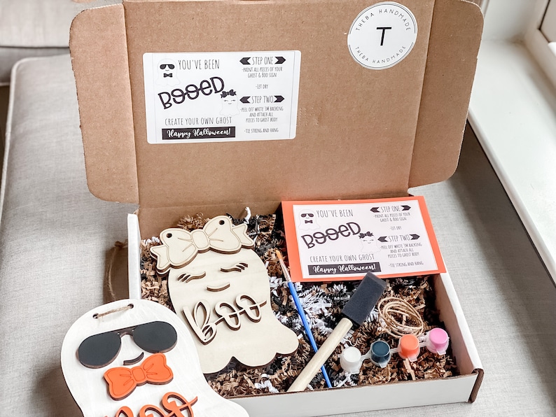 May include: A craft kit for creating your own ghost decorations. The kit includes two unfinished wooden ghost shapes, paint, brushes, and instructions. The instructions say "You've Been Booed!" and "Create Your Own Ghost! Happy Halloween!"