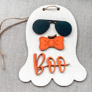 May include: A white wooden ghost with a black sunglasses, orange bow tie and the word "BOO" in orange letters.