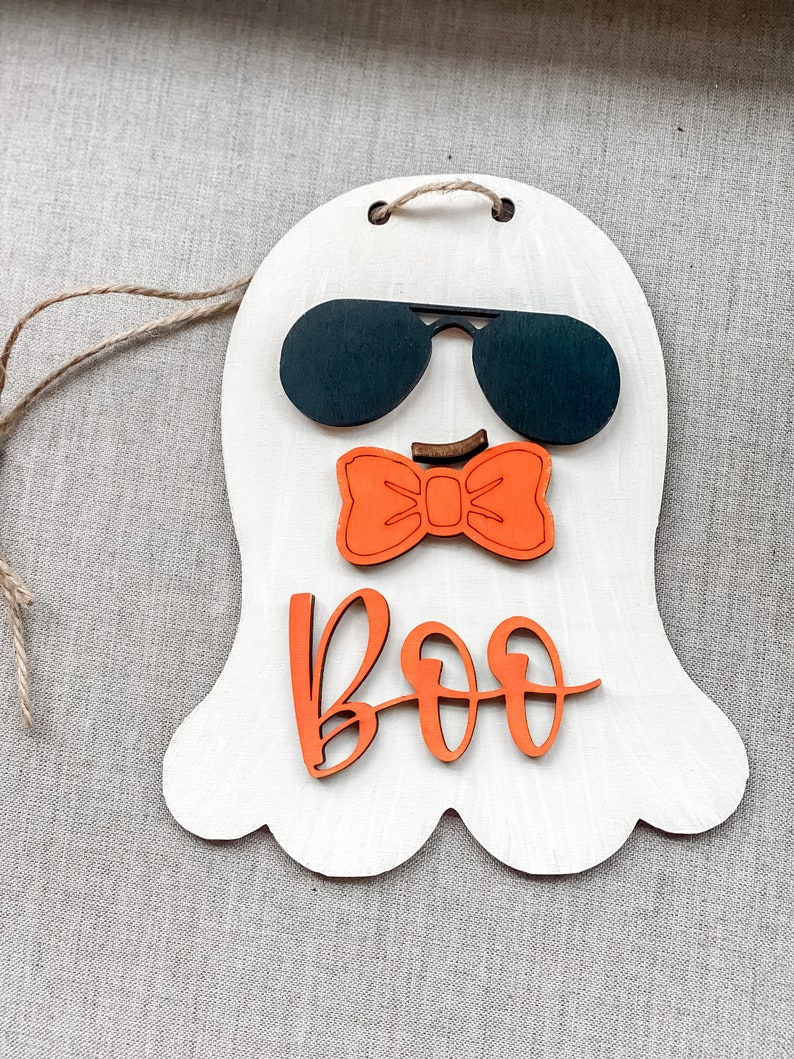 May include: A white wooden ghost with a black sunglasses, orange bow tie and the word "BOO" in orange letters.