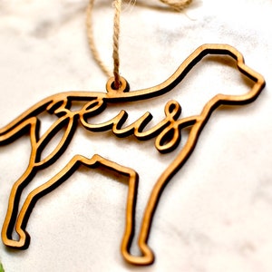 May include: Wooden ornament shaped like a dog with the word "Jesus" cut out inside. The ornament is brown and has a string for hanging.