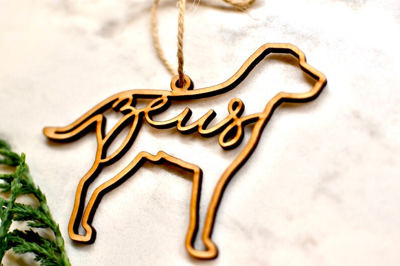 May include: Wooden ornament shaped like a dog with the word "Jesus" cut out inside. The ornament is brown and has a string for hanging.