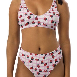 Puede incluir: Un bikini rosa y blanco con estampado de fresas. La parte superior del bikini tiene un escote redondo y tirantes ajustables. La parte inferior del bikini tiene un corte de cintura alta.
