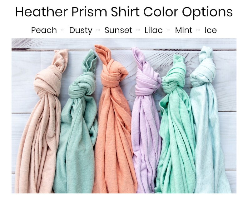 May include: Six folded t-shirts in different pastel colors: peach, dusty green, sunset orange, lilac, mint green, and ice blue. The t-shirts are arranged in a row on a white wooden surface.  Peach - Dusty - Sunset - Lilac - Mint - Ice