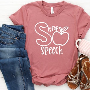 May include: A dusty rose t-shirt with white text that reads "S is for Speech" with a stylized apple graphic.