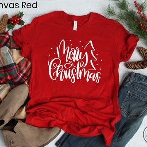 Puede incluir: Una camiseta roja con texto blanco que dice "Feliz Navidad" con un gr&aacute;fico de &aacute;rbol de Navidad estilizado.