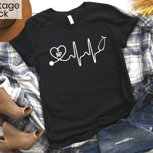 May include: Black t-shirt with a white graphic of a stethoscope, heart, and heartbeat line with the letters "NP" inside the heart.