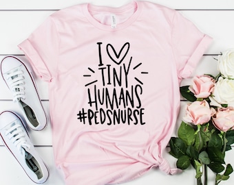 May include: Pink t-shirt with black text that reads "I love tiny humans #pedsnurse".