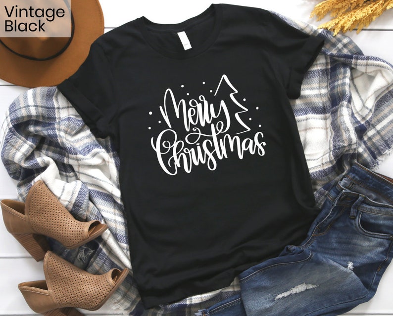 Puede incluir: Camiseta negra con un gr&aacute;fico blanco que dice "Feliz Navidad" con un &aacute;rbol de Navidad estilizado.