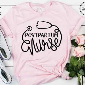 May include: A soft pink t-shirt with a black graphic that says "Postpartum Nurse" with a stethoscope and heart design.