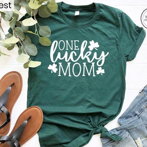 May include: A green t-shirt with the text "One Lucky Mom" in white lettering and shamrock designs.