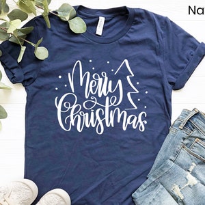 Puede incluir: Una camiseta azul marino con un gr&aacute;fico blanco que dice "Feliz Navidad" con un &aacute;rbol de Navidad estilizado.