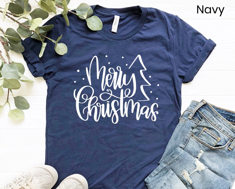 Puede incluir: Una camiseta azul marino con un gr&aacute;fico blanco que dice "Feliz Navidad" con un &aacute;rbol de Navidad estilizado.
