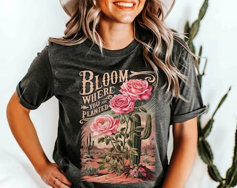 May include: A dark gray t-shirt with a vintage-style graphic featuring pink roses, a cactus, and the text "Bloom Where You Are Planted".