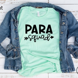 May include: A mint green t-shirt with black text that reads "PARA squad" with arrows on either side of the word "squad".