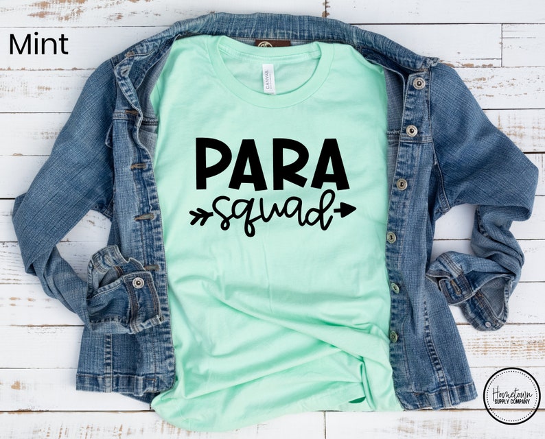 May include: A mint green t-shirt with black text that reads "PARA squad" with arrows on either side of the word "squad".