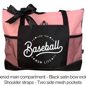 Op de afbeelding: Roze en zwarte tote bag met een zwarte satijnen strik. De tas heeft een ritsvak, twee zijvakken van mesh en een zwart vak met de tekst "Livin' That Baseball Mom Life" in wit.