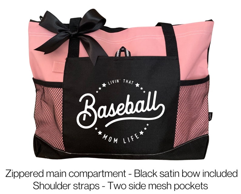 Op de afbeelding: Roze en zwarte tote bag met een zwarte satijnen strik. De tas heeft een ritsvak, twee zijvakken van mesh en een zwart vak met de tekst "Livin' That Baseball Mom Life" in wit.