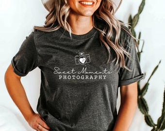 May include: A dark gray t-shirt with a white camera and heart graphic and the text "Sweet Moments Photography".