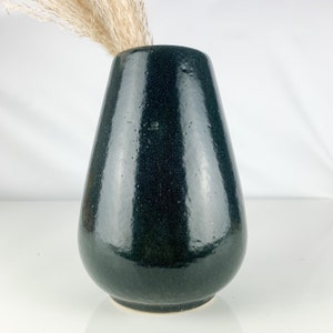 May include: A dark green ceramic vase with a rounded, pear-shaped body. The vase has a smooth, glossy finish.