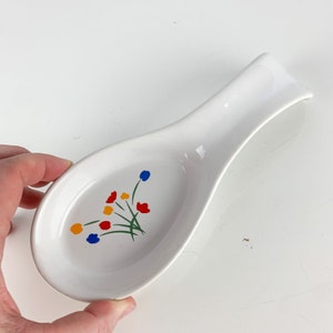 May include: White ceramic spoon rest with a floral design featuring red, yellow, blue, and green flowers.