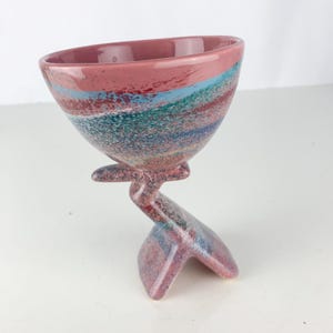 May include: A pink ceramic bowl with a swirling pattern of blue, green, and red. The bowl is on a unique, abstract, pink ceramic stand.