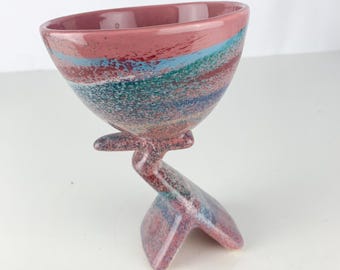 May include: A pink ceramic bowl with a swirling pattern of blue, green, and red. The bowl is on a unique, abstract, pink ceramic stand.