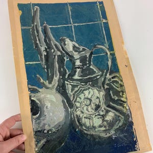 May include: An original painting featuring a still life composition. The artwork depicts a silver pitcher with a spiral design, a round object, and a hand against a blue tiled background. Signed by the artist, John T. Curtin.
