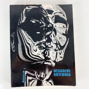 May include: Black and white cover of a book titled "DESIGNERS NOTEBOOK" with the word "ROCKUS" printed vertically on the left side.