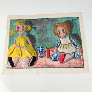 May include: A vintage print featuring two seated dolls with rosy cheeks and detailed features. One doll wears a yellow dress, the other a blue patterned dress with an apron. A blue and white tea set sits between them, on a pink and blue background.