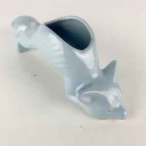 May include: A light blue ceramic fox-shaped planter. The fox is depicted in a downward-facing pose with an open container on its back. The planter has a glossy finish and is set against a white background.