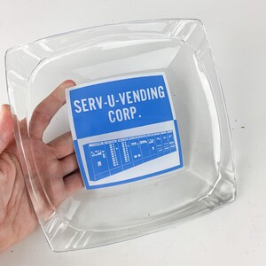 May include: A clear glass serving dish with a blue and white label that reads "SERV-U-VENDING CORP."