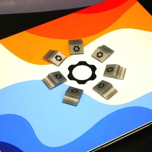 Puede incluir: Conjunto de pequeños componentes metálicos plateados, cada uno con un diseño en forma de engranaje, dispuestos alrededor de un objeto negro en forma de engranaje. Fondo colorido con tonos naranja, blanco y azul.