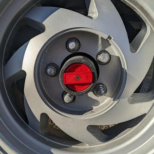 May include: Close-up of a silver alloy wheel with a red center cap. The wheel has a multi-spoke design with visible lug nuts and a central hub. The red cap has the word "FREE" and "LOCK" printed on it.