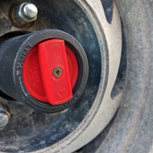 May include: Close-up of a black and red 4x4 wheel hub lock. The red locking mechanism is in the locked position, with the word "LOCK" visible. The hub is surrounded by a silver wheel and lug nuts.