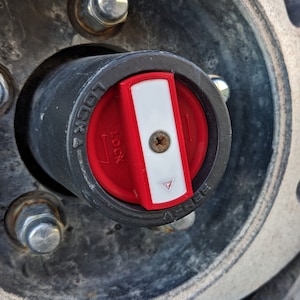 Puede incluir: Primer plano de un bloqueo de cubo de rueda negro y rojo. El dial rojo tiene una franja blanca y está marcado con "LOCK" y "FREE". Un pequeño tornillo está en el centro. El cubo está rodeado por una rueda de metal.